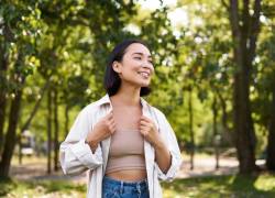 Foto de mujer sonriente ubicada un espacio de naturaleza, practicando mindful walking.