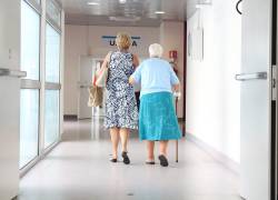 Adulta mayor camina junto a mujer más joven en un hospital.