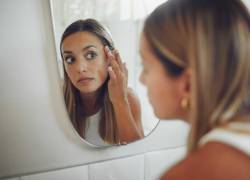 Foto de una mujer observando su rostro en el espejo. Algunas manchas faciales pueden deberse a la exposición solar sin protección.