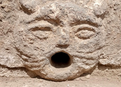 Una pared de piedra en la que fue tallado un rostro boquiabierto, de cientos de años de antiguedad.