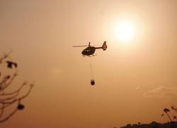 Fotografía que muestra a un helicóptero asistiendo en las labores para apagar las llamas.