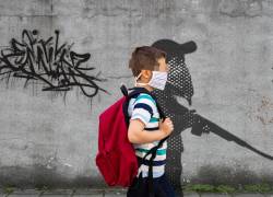 Un niño junto a un mural que simboliza su vulnerabilidad ante la captación de las bandas del crimen organizado en Ecuador.