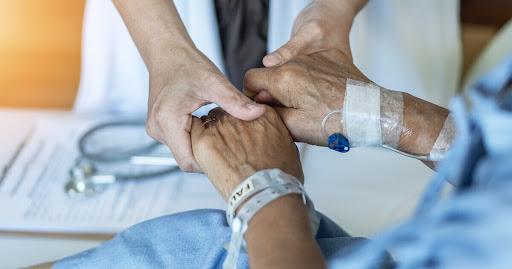 Familiar sostiene la mano de su paciente en un proceso de atención hospitalaria.