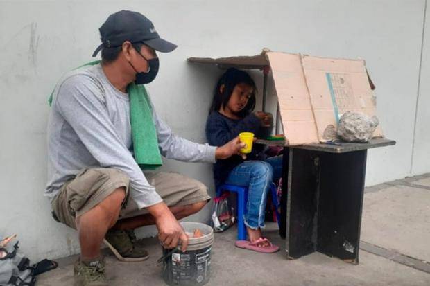 Niña conmueve al estudiar bajo una caja de cartón mientras su padre lava autos