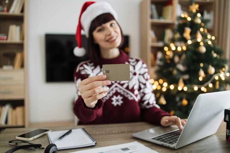 $!Mujer mostrando su tarjeta de crédito y frente a la computadora, lista para hacer compras navideñas online.