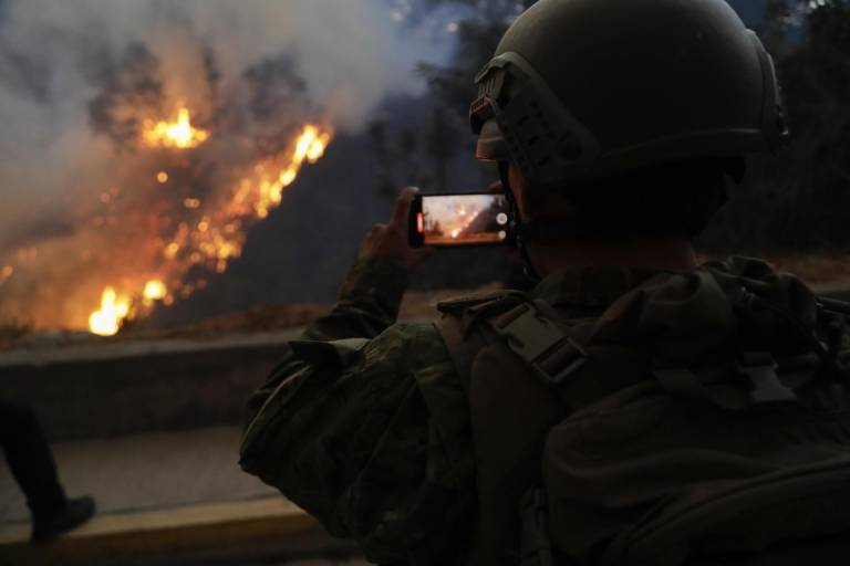 $!Un integrante del Ejército de Ecuador toma imágenes con su teléfono de un incendio forestal este martes, en el sector de Guápulo en Quito.