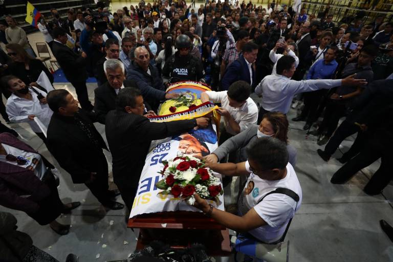 $!Varias personas colocan elementos como una banda con los colores patrios y un arreglo floral sobre el féretro del candidato Fernando Villavicencio, durante un velatorio público en un recinto ferial al que fue llevado previo a su entierro, hoy, en Quito (Ecuador).