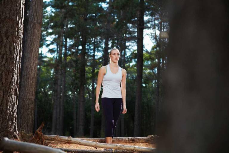 $!Una mujer caminando en medio de un bosque, su rostro denota cansancio.