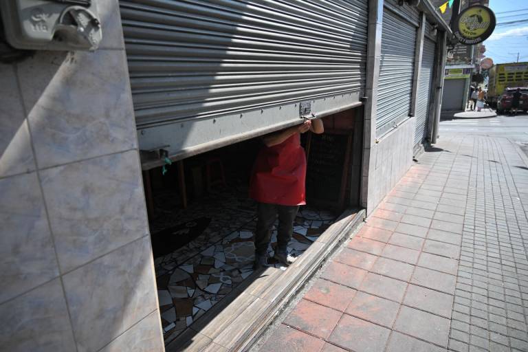 $!Una mujer cierra la puerta de un restaurante sin electricidad en Quito. Propietarios de negocios denuncian los desafíos de mantener sus negocios con los cortes de luz.