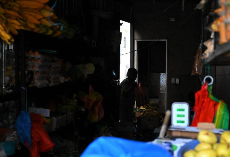 $!Una mujer acomoda frutas y vegetales en una tienda de Quito, en medio del corte de luz programado.