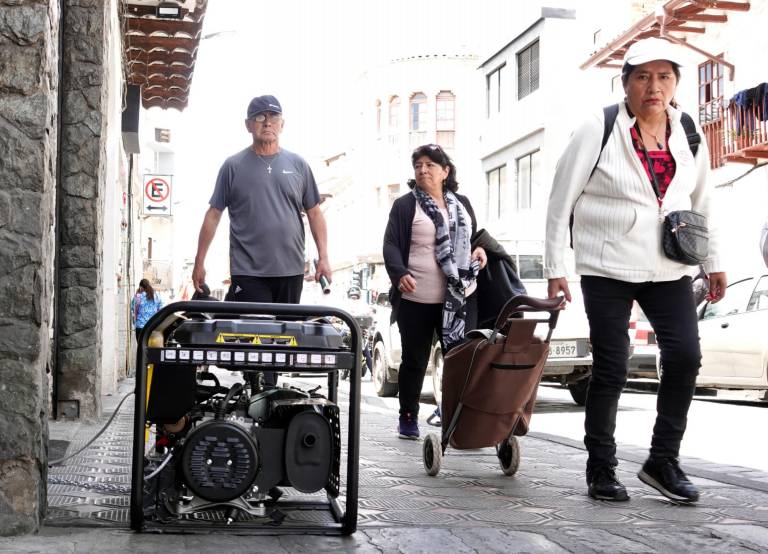 $!Ciudadanos caminando al lado de un generador que alimenta de electricidad a un local comercial, en una calle de Cuenca.